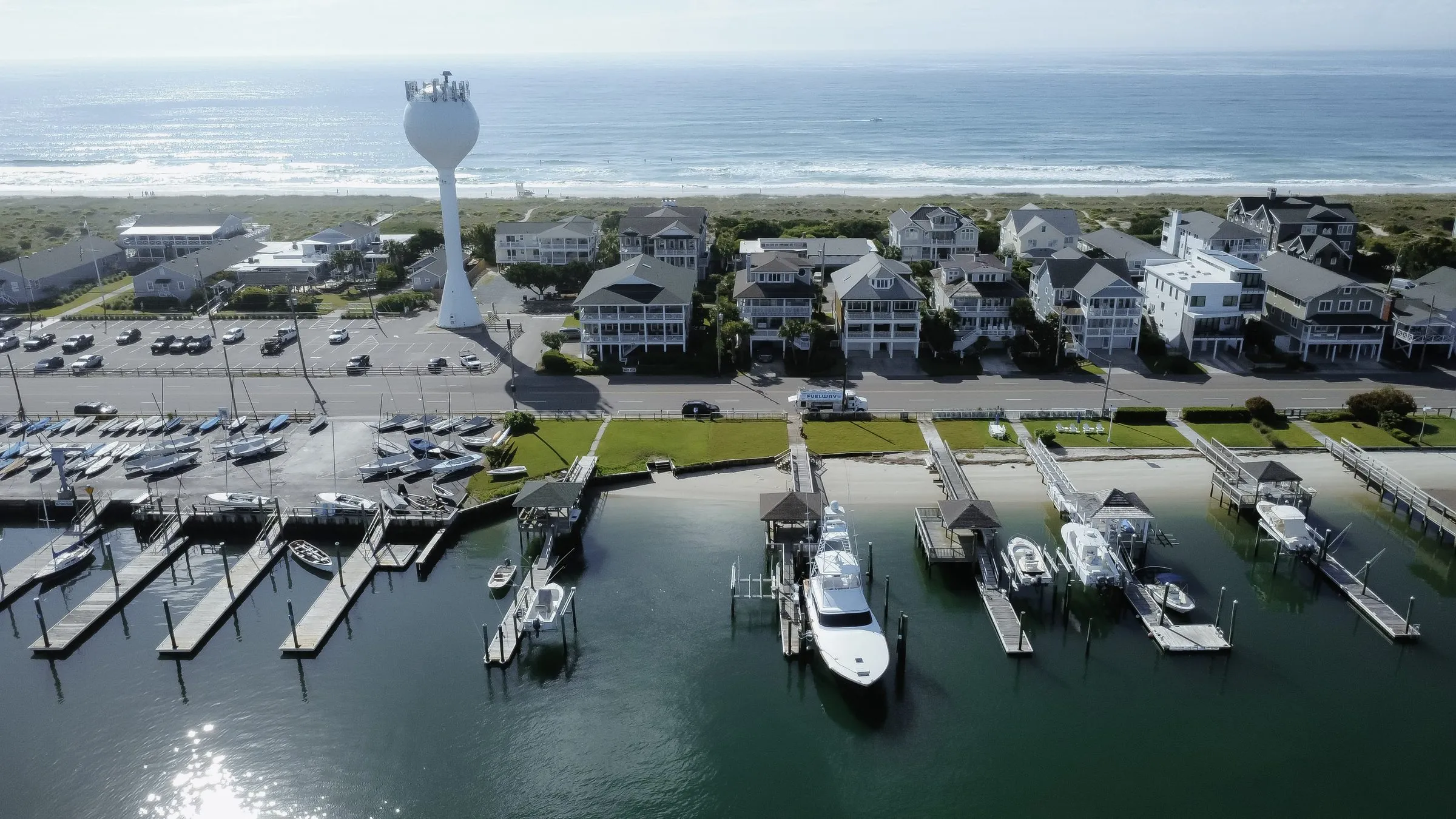 A coastal marina from the air, sailboats and slips in the foreground and the Atlantic behind the beachfront houses