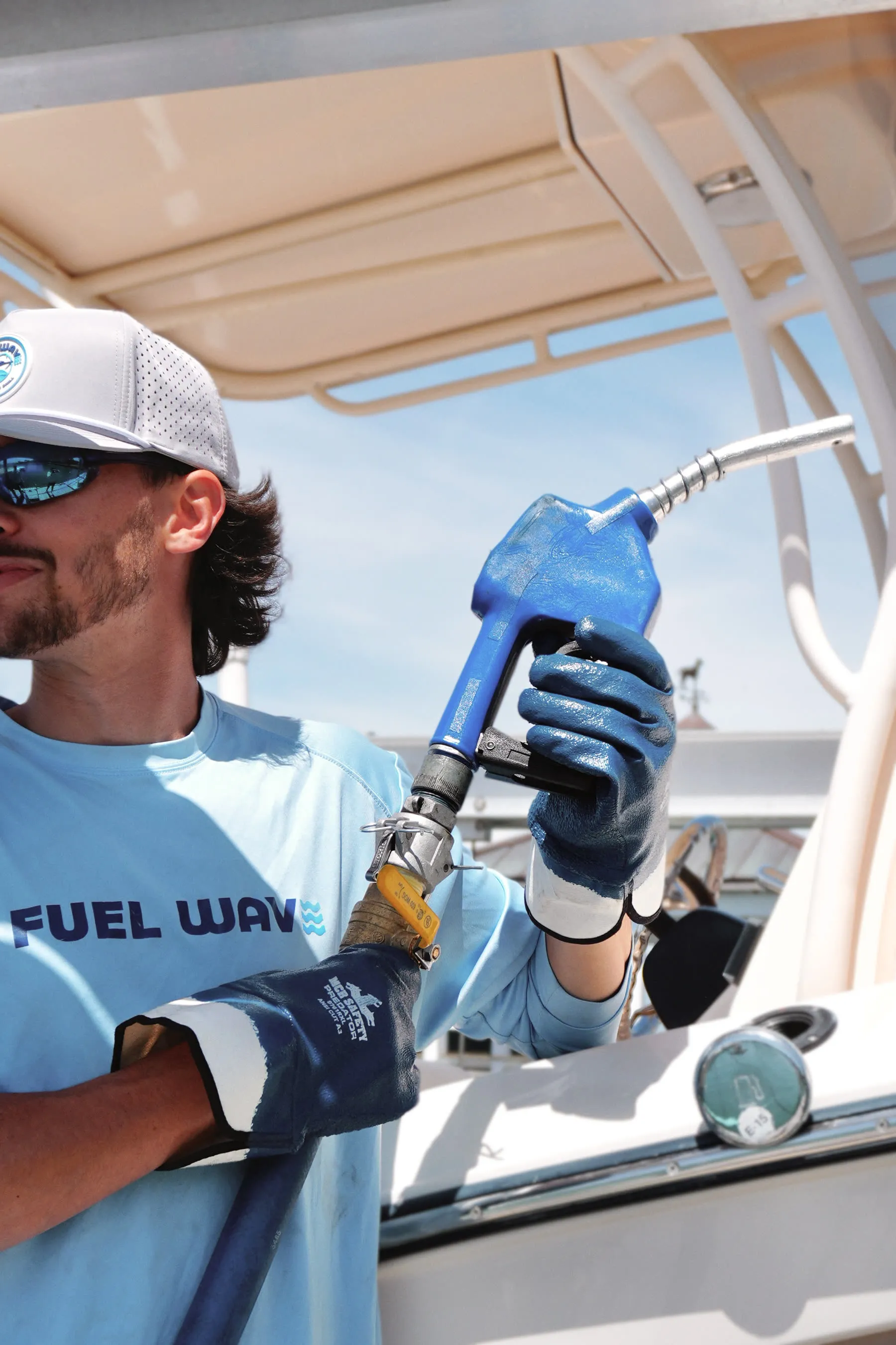 A Fuel Wave crew member under the T-top of a center console, holding the blue marine nozzle