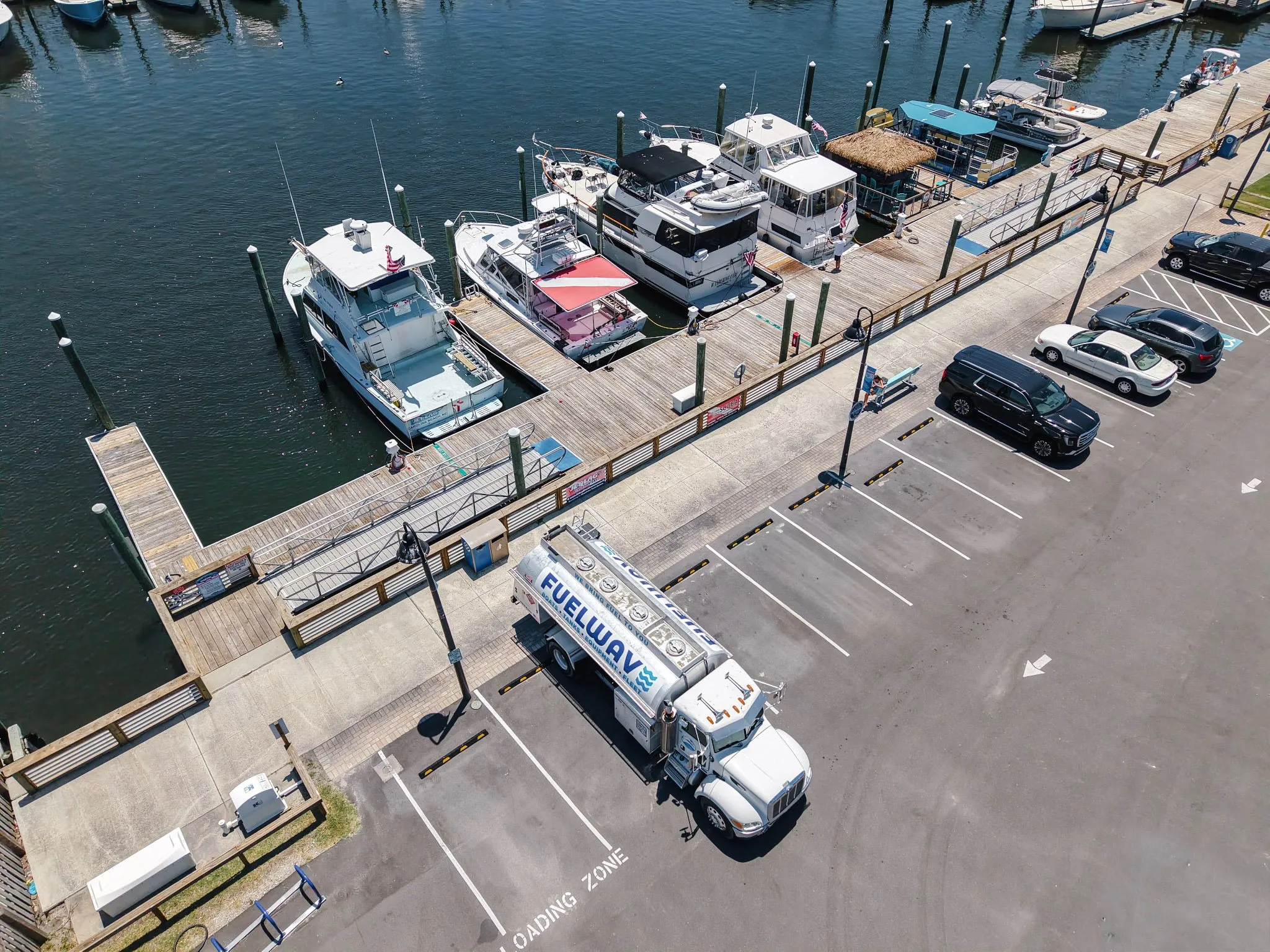 The Fuel Wave tanker parked in a marina lot beside the boardwalk, sportfishers and cruisers tied up in the slips, seen from above