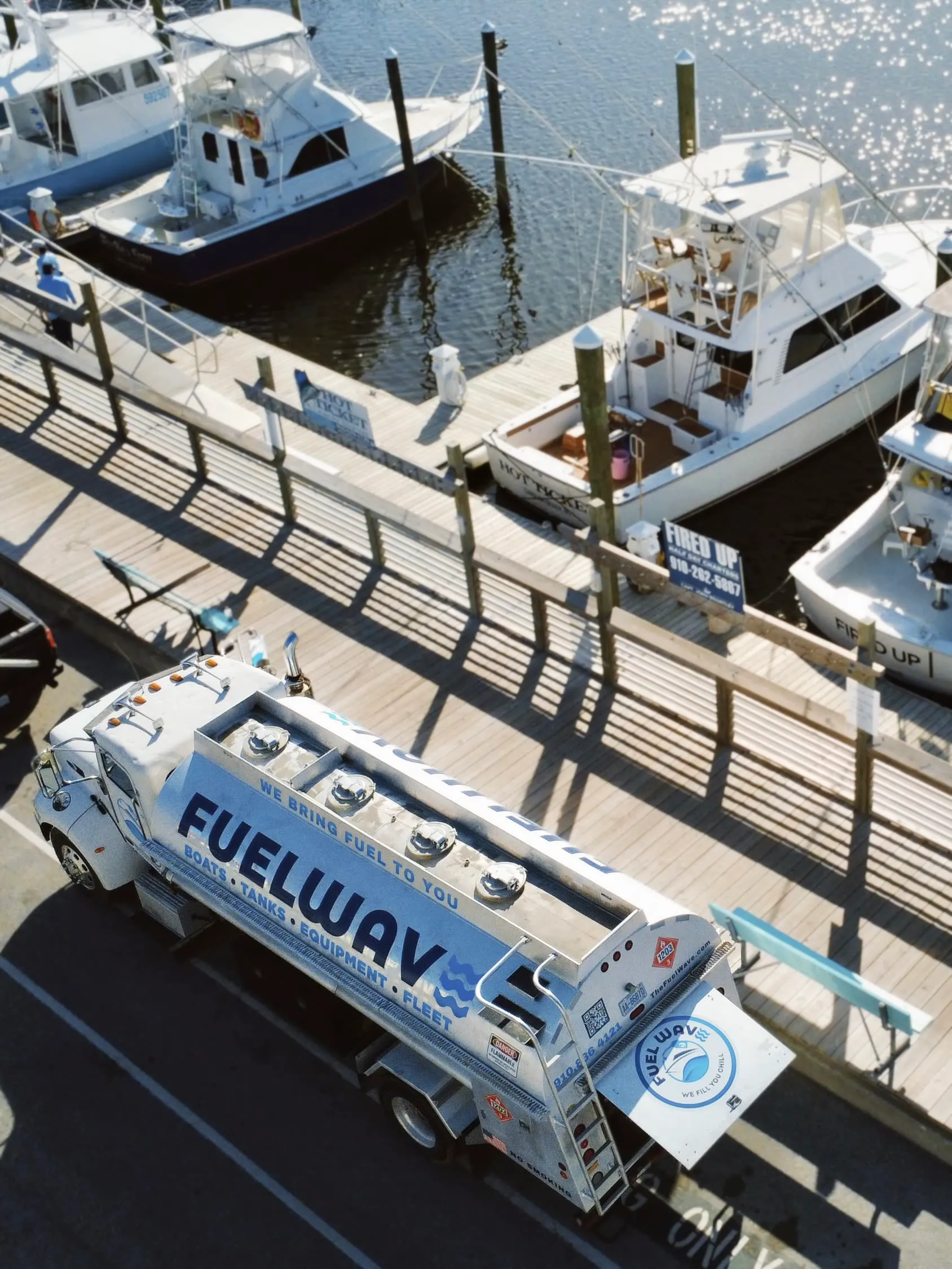 The Fuel Wave tanker on the lot beside a marina dock, sportfishers tied up alongside, seen from above