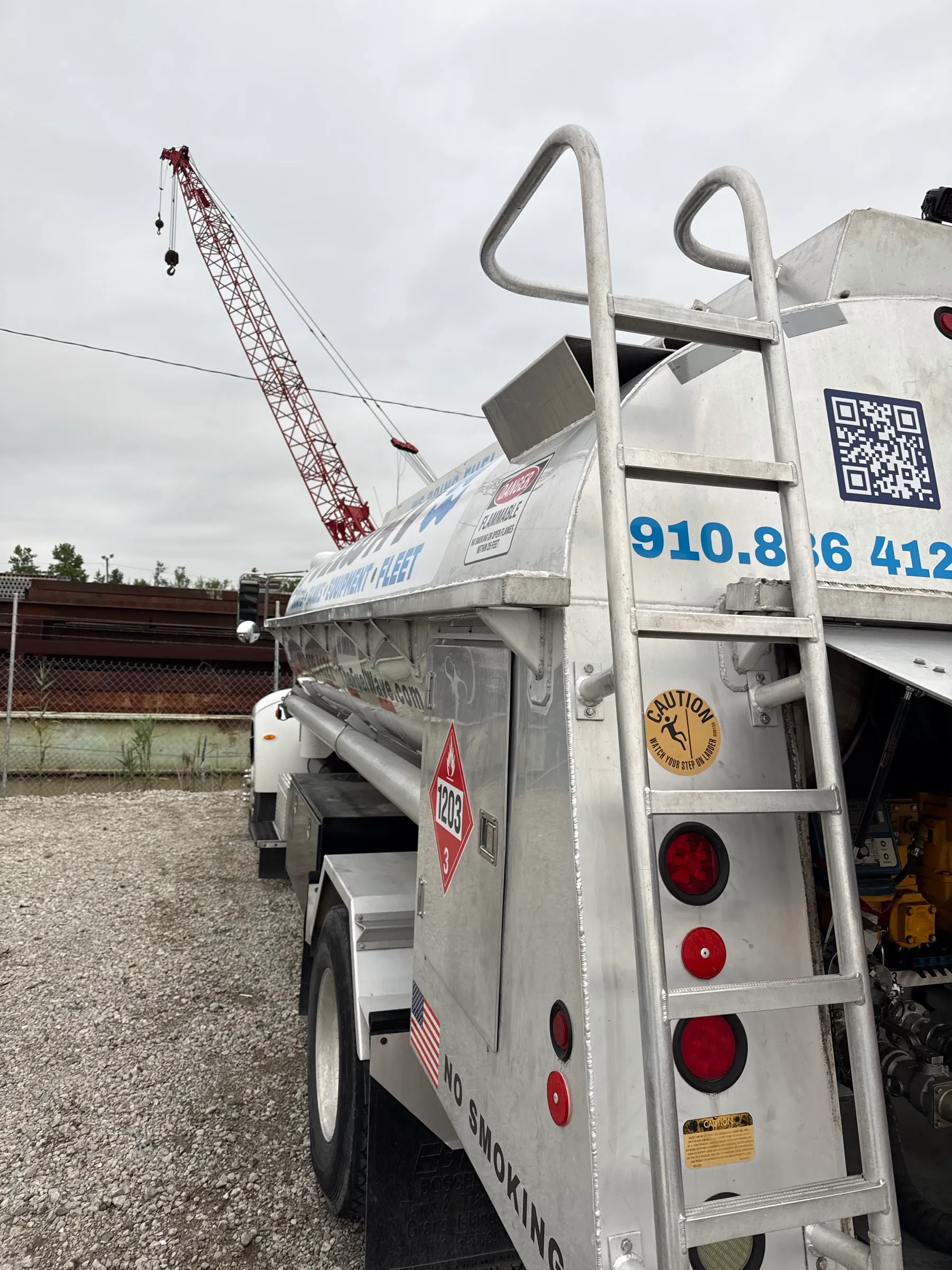 The rear of the Fuel Wave tanker on a gravel job site, with its ladder up the tank and a crawler crane behind it