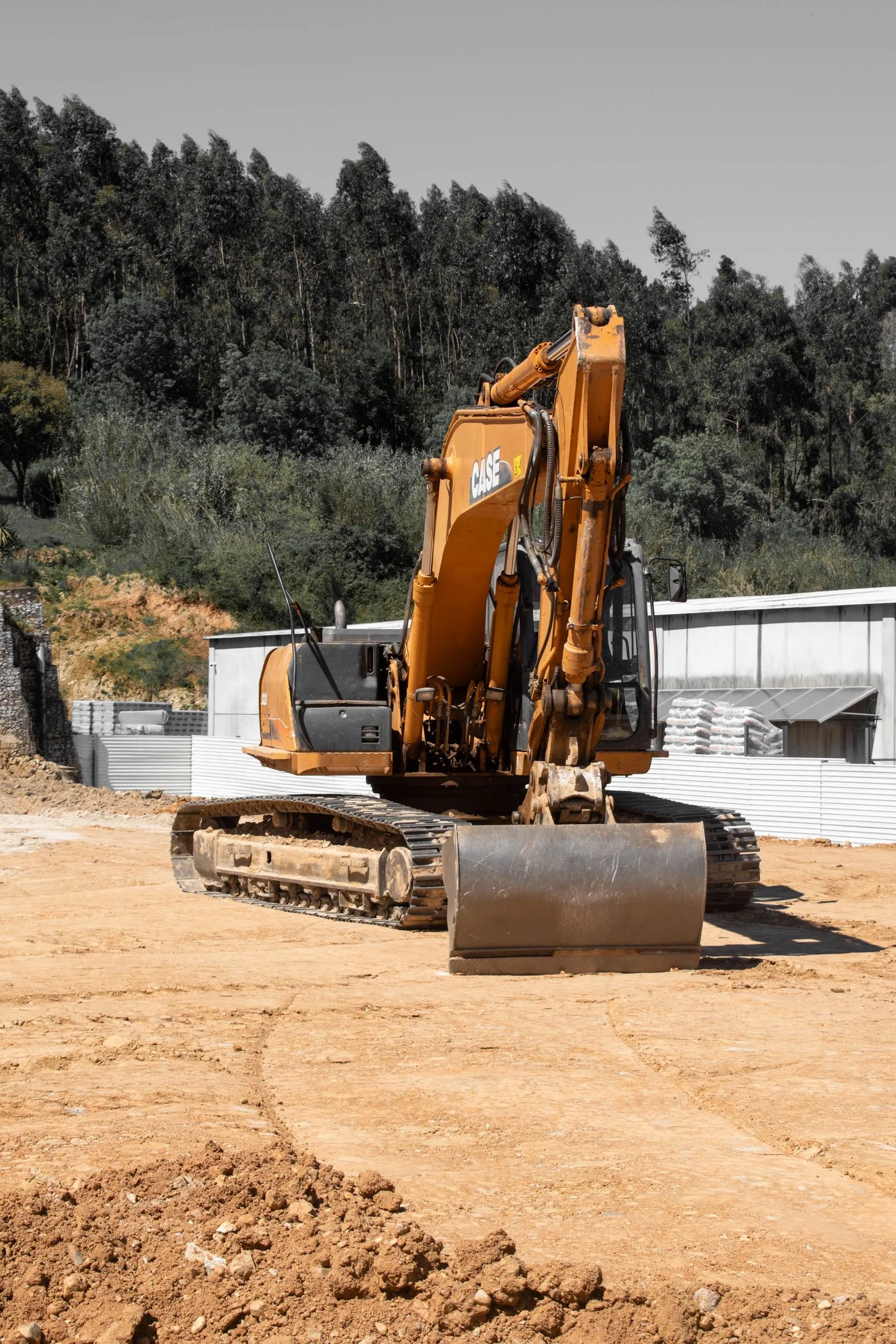 An orange tracked excavator on a sandy job site, pines behind it